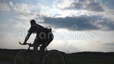 年轻人骑着老式自行车的剪影，背景是美丽的日落天空。 在乡下骑自行车